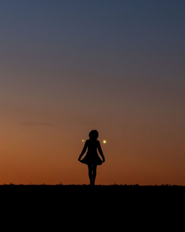 黎明时分，一名女子的剪影，身后是两颗明亮的行星。作者：Marek Nikondem